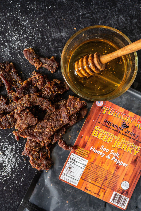 A photo of Sea Salt, Honey and Pepper Brisket Beef Jerky with seasonings and a small dipping bowl of honey